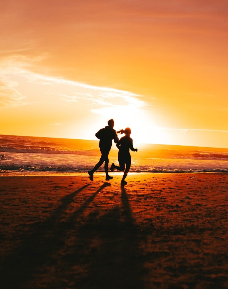 a couple of people running on a beach at sunset